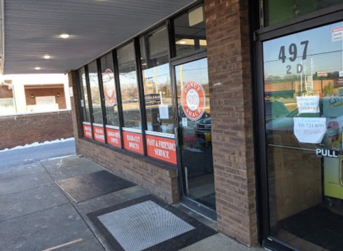 Exterior view of a restaurant with large windows and signage, featuring a door and a sidewalk in front.