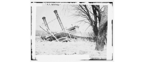 A historic steamboat, the H.M. Bedford, partially submerged in ice, with two tall smokestacks visible.