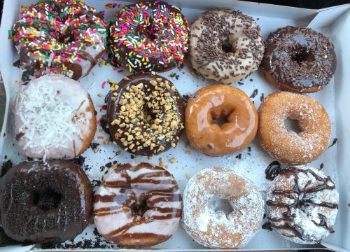 A box of assorted donuts, featuring various toppings like sprinkles, chocolate, nuts, and coconut.