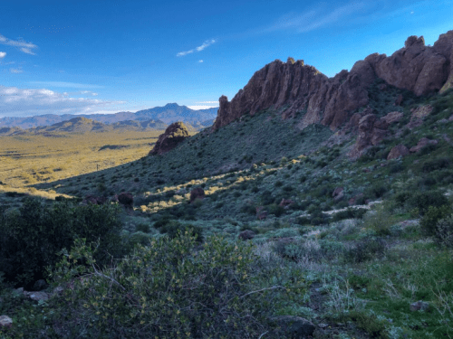 A scenic view of rugged mountains and green hills under a blue sky with scattered clouds.