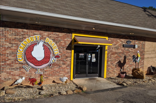 Exterior of Chickenbutt Donuts featuring a colorful sign, brick wall, and decorative chickens in front.