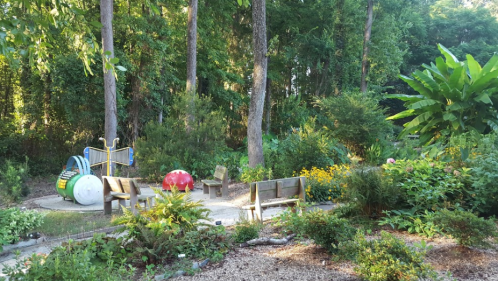 A serene park scene with colorful play equipment, benches, and lush greenery surrounded by trees and flowers.