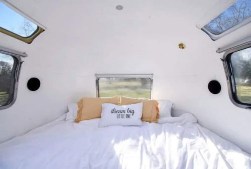 Cozy interior of a camper with a large bed, white bedding, and a decorative pillow that says "dream big little one."