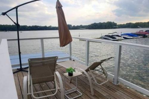 A serene lakeside deck with two lounge chairs, a small table, and an umbrella overlooking the water and boats.