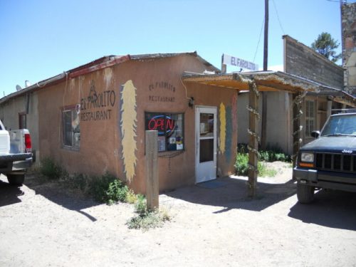 A rustic restaurant building with a sign reading "El Parito" and an open door, surrounded by parked vehicles.