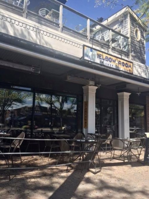 Exterior view of the Elbow Room restaurant, featuring outdoor seating and large windows on a sunny day.