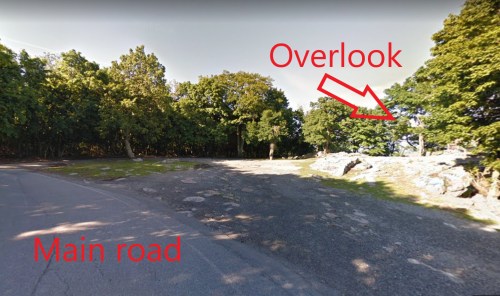 A view of a main road with an overlook area surrounded by trees and rocks.