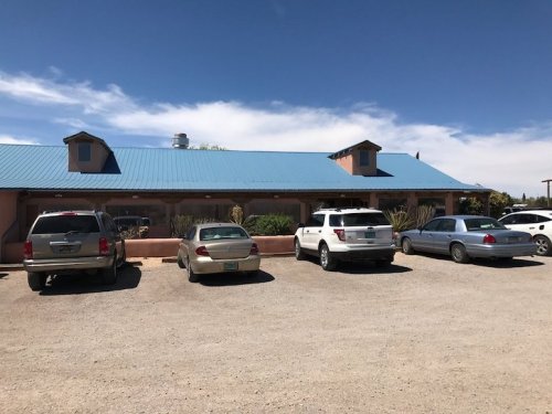 A row of parked cars in front of a single-story building with a blue roof under a clear blue sky.