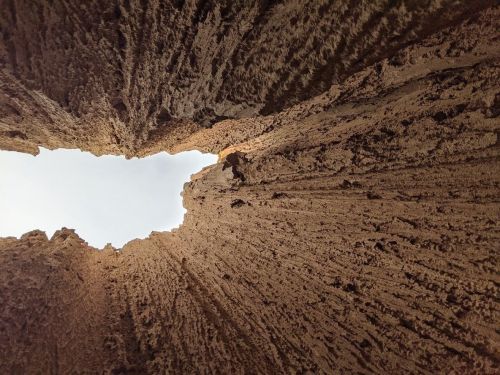 View looking up from a narrow canyon, with textured rock walls and a glimpse of blue sky above.