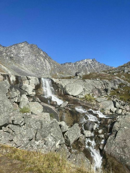 A serene mountain landscape featuring a waterfall cascading over rocks under a clear blue sky.
