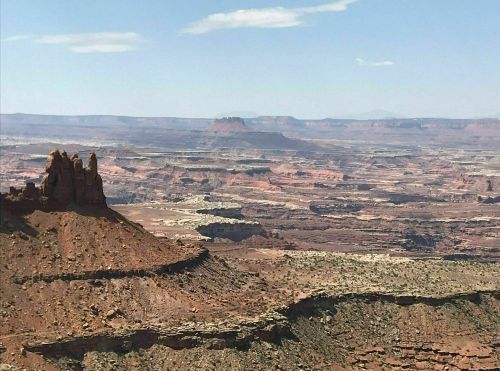 A vast desert landscape with layered rock formations and distant mountains under a clear blue sky.