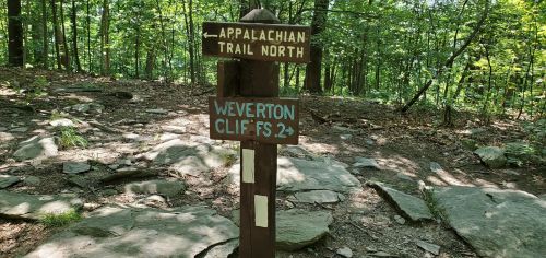 Trail sign in a wooded area indicating directions to Appalachian Trail North and Weverton Cliffs.