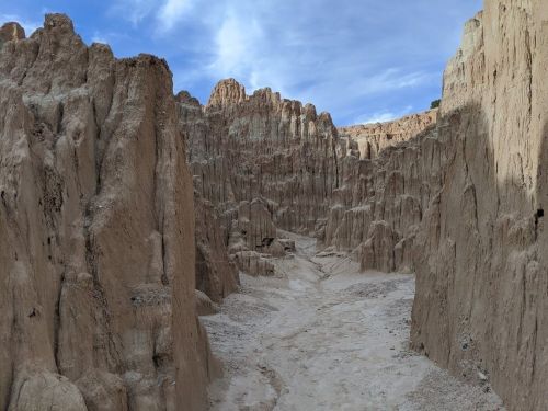 A rugged canyon with steep, sandy walls under a blue sky, showcasing natural erosion patterns.