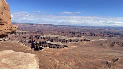 A vast desert landscape with rocky formations and distant mountains under a blue sky with scattered clouds.