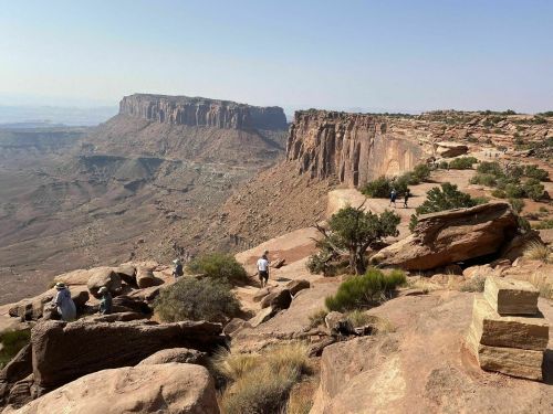 A scenic view of rocky cliffs and a vast canyon, with hikers exploring the landscape under a clear blue sky.
