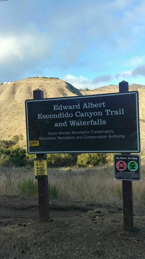 Sign for Edward Albert Escondido Canyon Trail and Waterfalls, with mountains in the background and warning symbols.