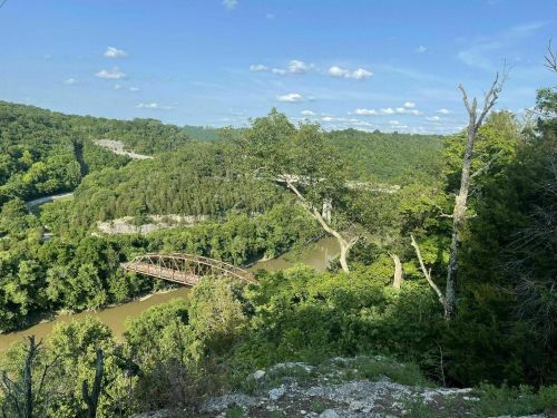A scenic view of a river winding through lush green hills, with a bridge crossing over the water under a blue sky.