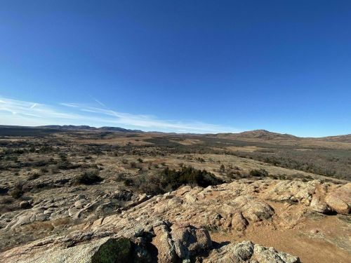A panoramic view of a rocky landscape under a clear blue sky, with distant hills and sparse vegetation.