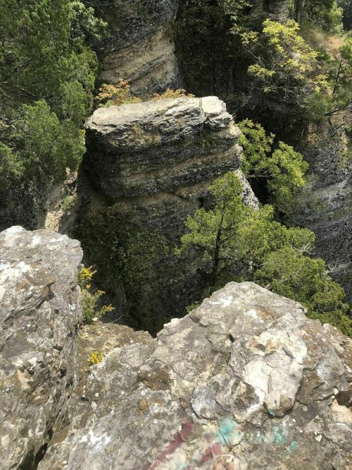 A rocky cliff with a flat-topped formation surrounded by trees and steep, rugged terrain.
