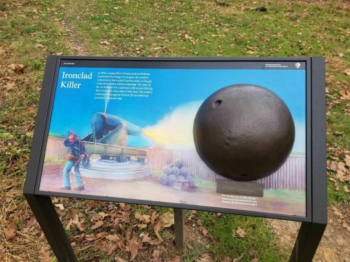 Sign depicting an ironclad cannonball and a soldier, with historical context about its use in battle.
