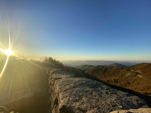 A scenic view of mountains at sunset, with sunlight shining over rocky terrain and a winding road in the distance.