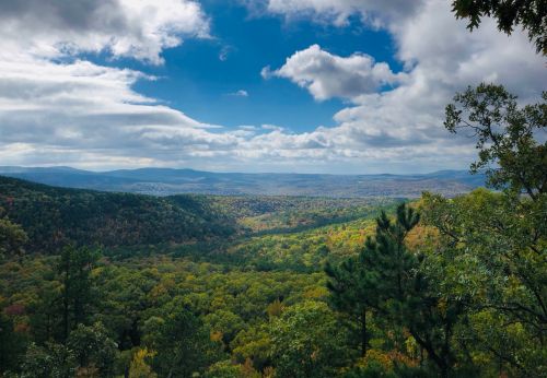 A panoramic view of a lush green valley surrounded by mountains under a partly cloudy sky.