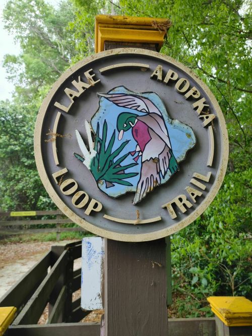 Sign for Lake Apopka Loop Trail featuring a colorful illustration of a bird among plants.