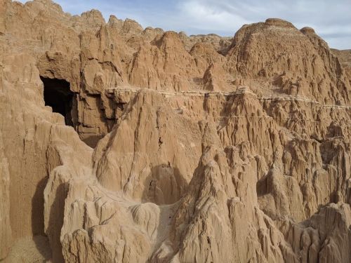 A rugged landscape of towering, eroded rock formations in a desert setting under a cloudy sky.
