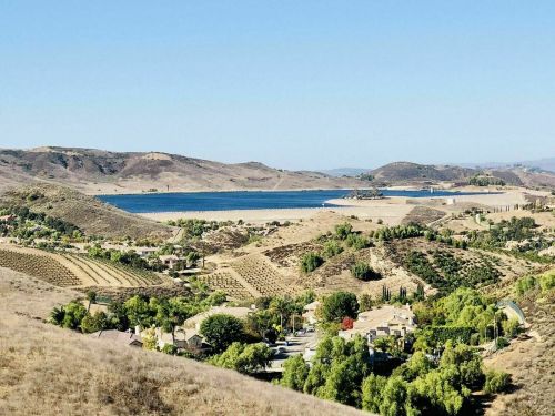 A scenic view of rolling hills, a lake, and lush greenery, with homes nestled in the foreground under a clear blue sky.