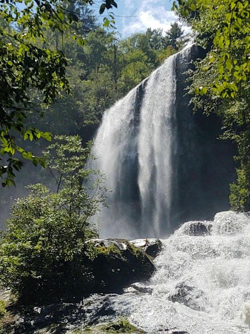 A cascading waterfall surrounded by lush greenery and sunlight filtering through the trees.