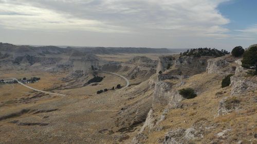 A vast landscape featuring rolling hills, cliffs, and a winding road under a cloudy sky.