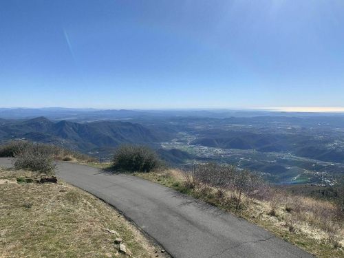 A winding path leads to a panoramic view of mountains and valleys under a clear blue sky.