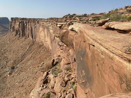 A rugged cliffside with layered rock formations and sparse vegetation under a clear blue sky.