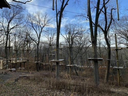 A treetop adventure course with wooden platforms and ropes suspended between trees, set in a wooded area.