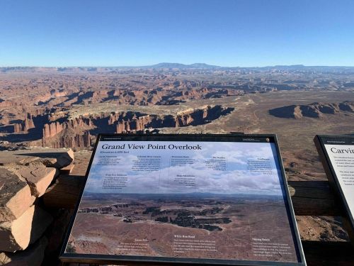 A scenic view from Grand View Point Overlook, showcasing vast canyons and distant mountains under a clear blue sky.