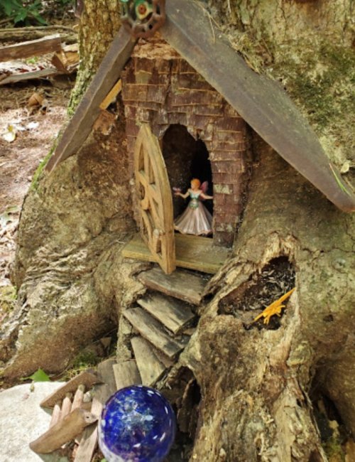 A whimsical fairy house built into a tree trunk, with a small figure and a blue glass orb nearby.