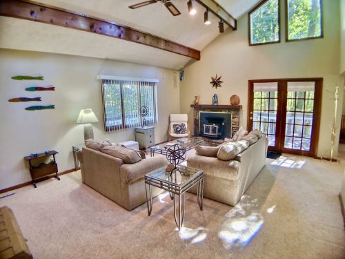 Cozy living room with high ceilings, large windows, and comfortable seating, featuring a fireplace and natural light.