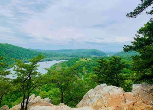 Scenic view of a lush green valley with a river, framed by rocky outcrops and trees under a cloudy sky.