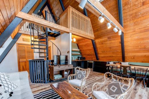 Cozy A-frame interior with wooden beams, spiral staircase, and a mix of seating areas and kitchen space.