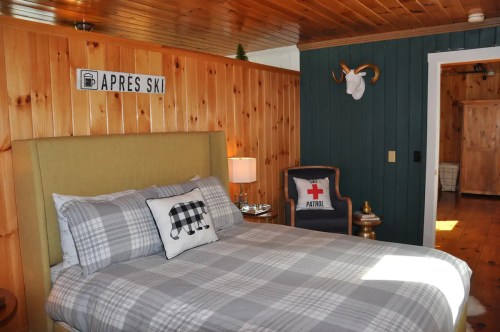 Cozy bedroom with wood paneling, a plaid bedspread, and ski-themed decor, including a sign and a mounted deer head.