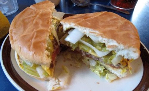 A close-up of a halved hamburger with pickles, onions, lettuce, and mustard on a plate.