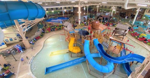 Aerial view of a vibrant indoor water park featuring slides, pools, and play structures with people enjoying the space.