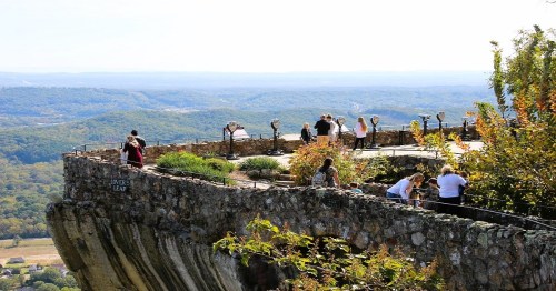 A scenic overlook with visitors enjoying the view of rolling hills and valleys under a clear sky.