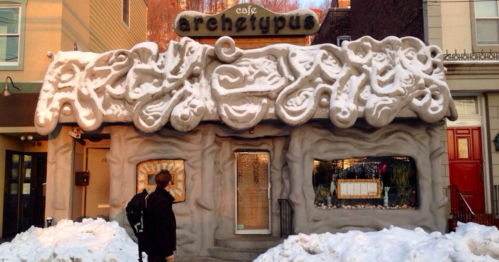 A whimsical café with a textured, sculptural exterior, surrounded by snow, and a person standing in front.