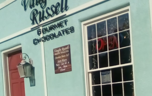 Exterior of a light blue shop with a sign reading "Vaughn Russell Gourmet Chocolates" and an "Open" neon sign.