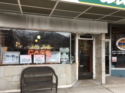 Exterior of a café with a neon sign, large windows displaying photos, and a stone bench outside.