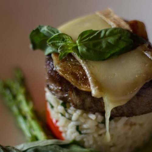 A gourmet dish featuring a beef fillet topped with cheese and basil, served on a bed of rice with asparagus.