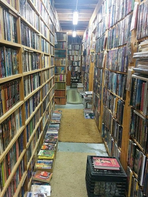 A narrow aisle lined with tall bookshelves filled with books, leading to a cozy reading area at the end.