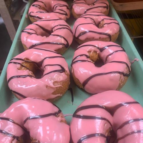 A tray of pink frosted donuts drizzled with chocolate, arranged in a neat row.