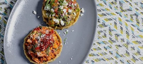 Two colorful tostadas topped with shredded chicken, green sauce, and cheese, served on a gray plate.